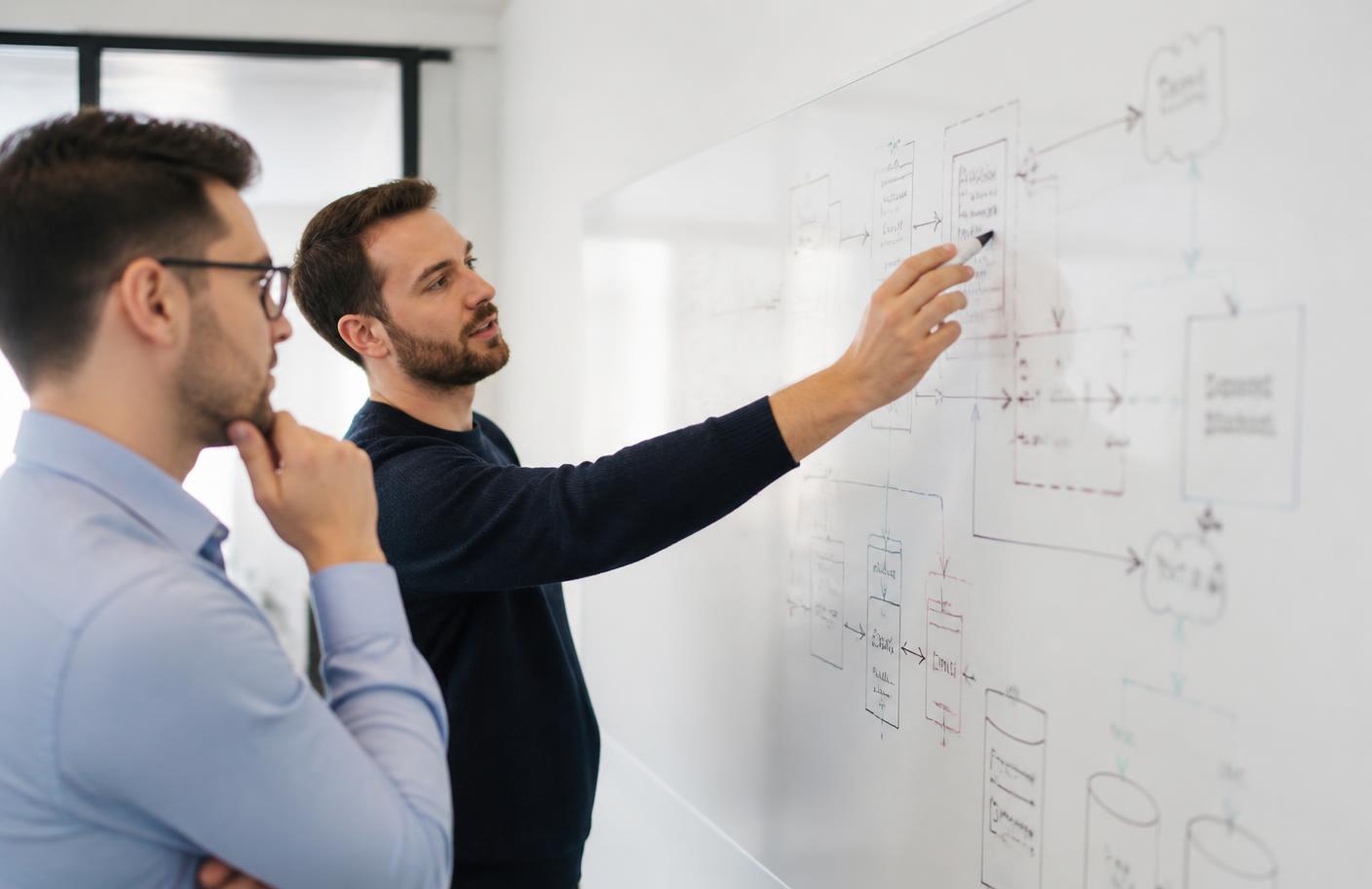 Two technology consultants discussing a system architecture diagram drawn on a whiteboard