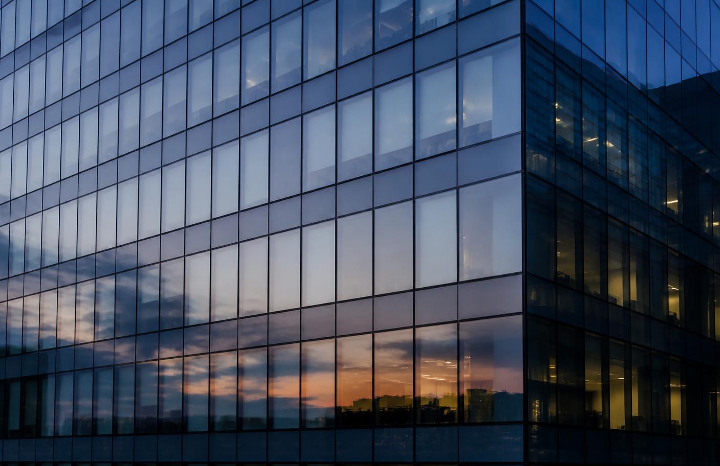 Glass facade of a modern office building at dusk reflecting a grid of sky and city lights